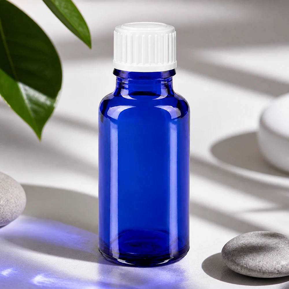 Apoteksflaska blå 20ml skruvkork vit standard Blå glasflaska på 20 ml med vitt lock bredvid naturstenar och gröna blad