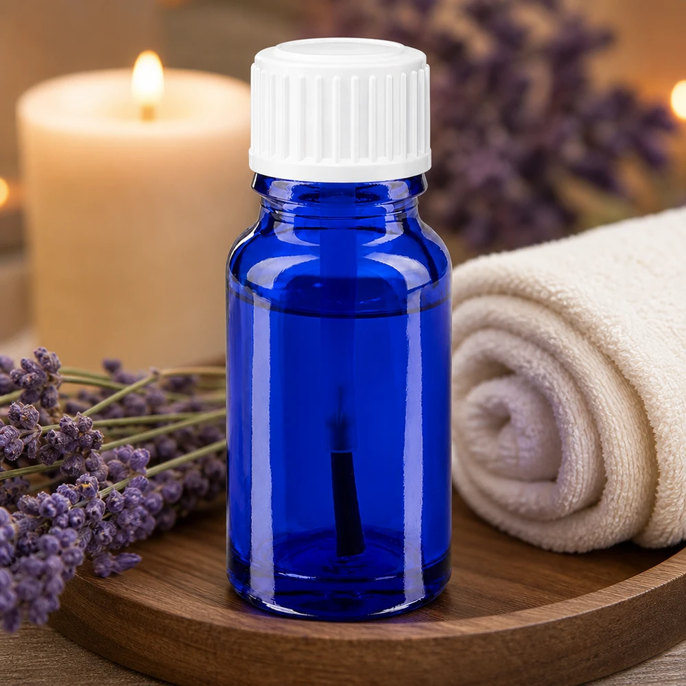 Apoteksflaska blå 10ml skruvlock vit borste Aromaterapiflaska, 10 ml, i blått apotekerglas med vit penselapplikator bredvid lavendelblommor