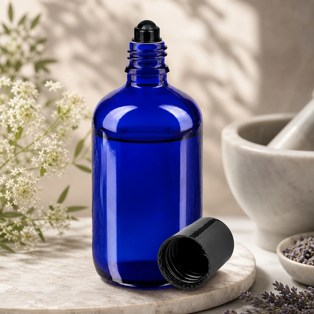 En koboltblå glasflaska på 100 ml med svart rullkula, öppen, bredvid lavendelblommor och en mortel