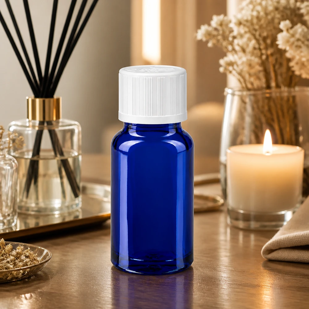 Apoteksflaska blå 10ml skruvkork vit barnsäker standard En liten blå glasflaska på 10 ml med vitt skruvlock på ett träbord bredvid en doftlampa och ett ljus