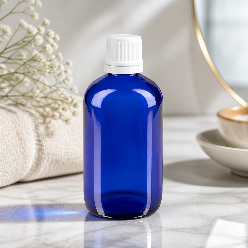 Apoteksflaska blå 100ml skruvkork vit manipulationsskyddad förslutning Blå glasflaska på 100 ml med vit OV-kork på marmor, bredvid en handduk och torkade blommor