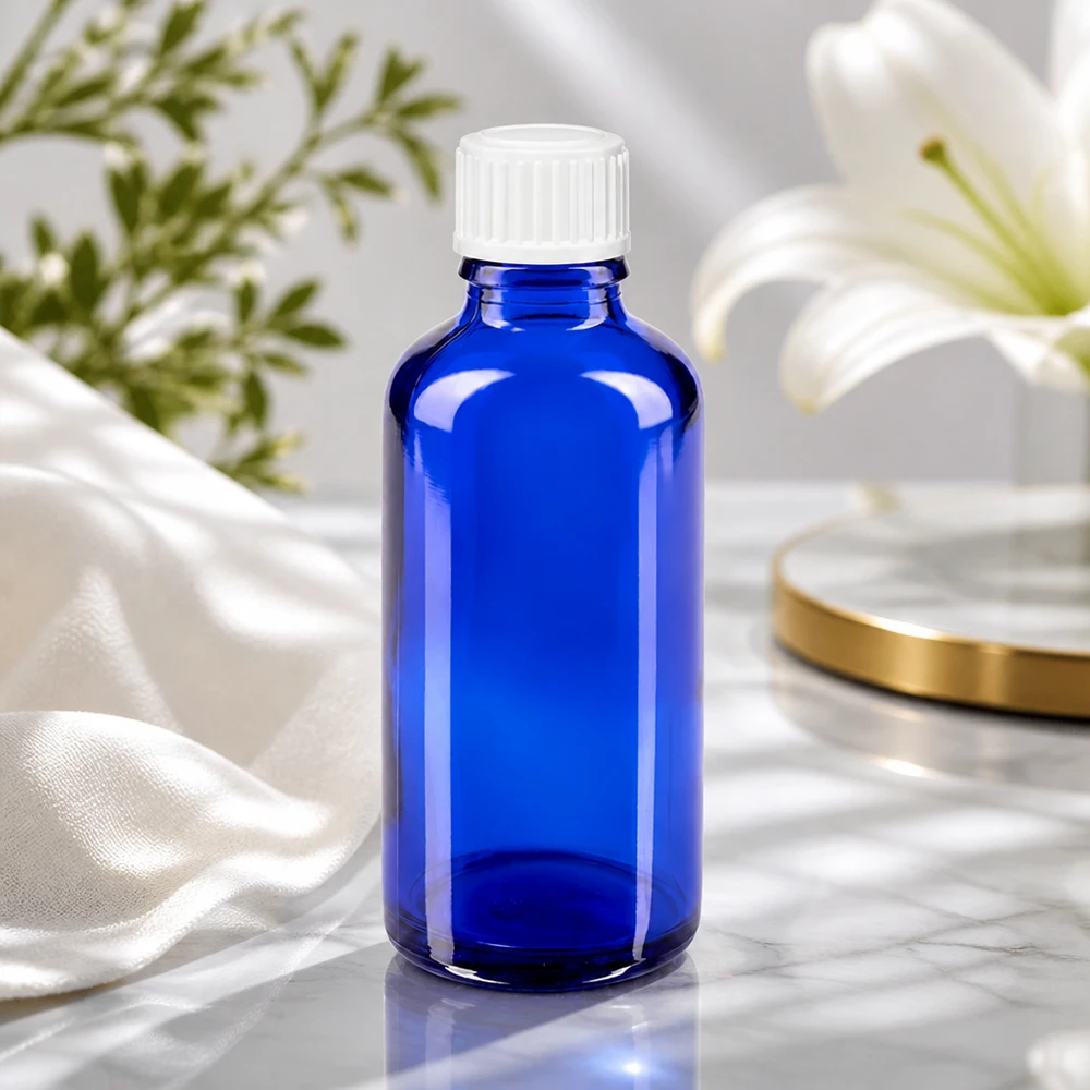 Apoteksflaska blå 50ml skruvkork vit standard Blå glasflaska på 50 ml med vitt skruvlock bredvid en vit lilja på en marmoryta