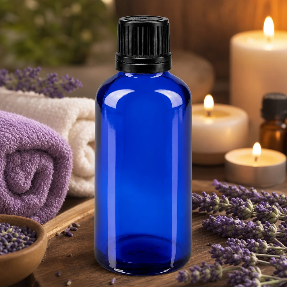 Blå glasflaska på 50 ml med svart droppkork, omgiven av lavendelblommor och ljus