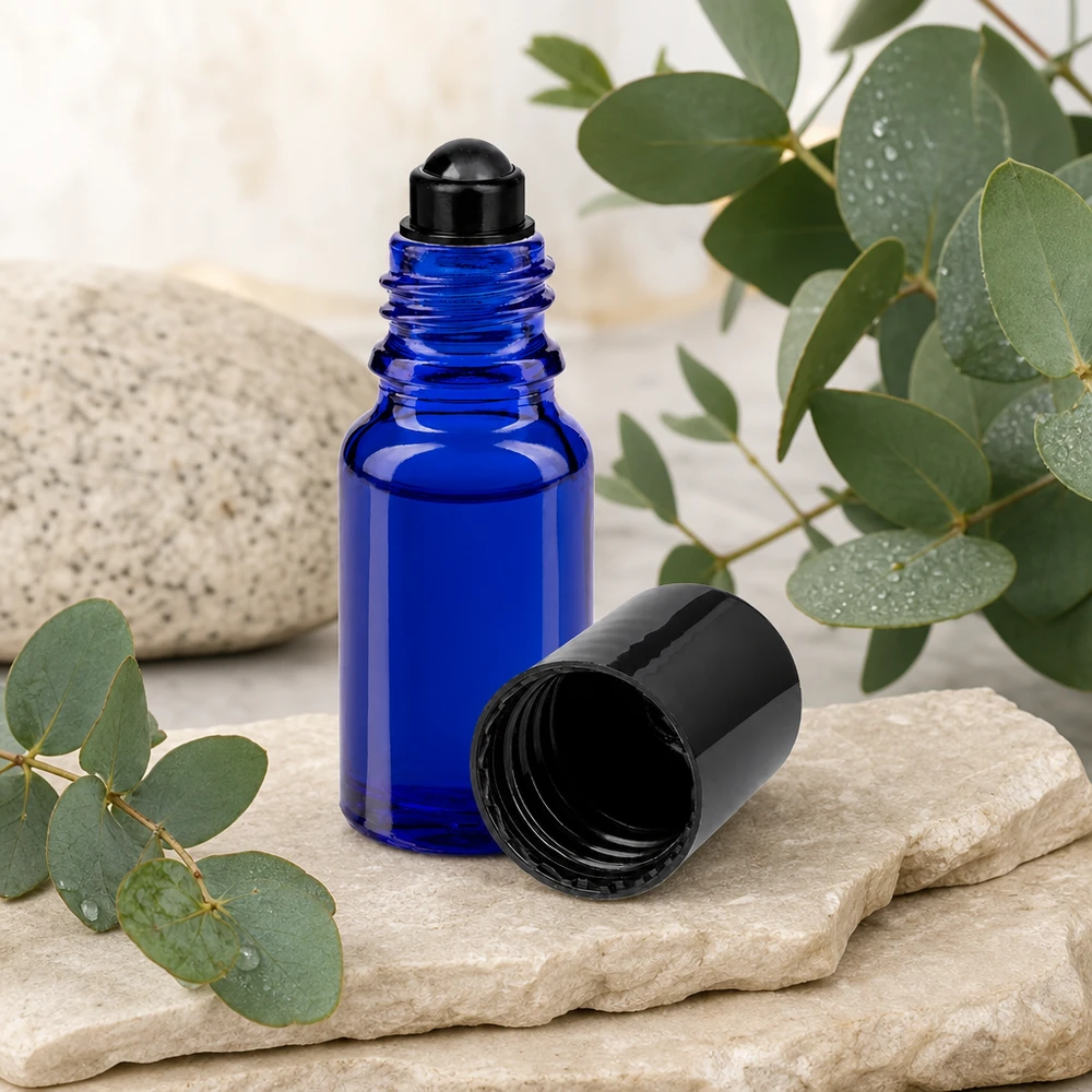 Blå 10 ml ApoGlas-roll-on-flaska med svart lock bredvid eukalyptusgrenar på natursten