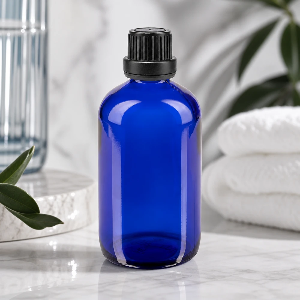 Apoteksflaska blå 100ml skruvkork svart säkerhetsförslutning Blå glasflaska på 100 ml med ett räfflat svart lock bredvid vita handdukar och gröna växter