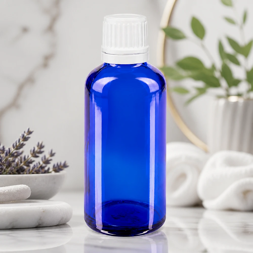 Apoteksflaska blå 50ml droppflaska 1,2mm vit barnsäker förslutning Blå glasflaska på 50 ml med vitt skruvlock på marmor bredvid lavendel