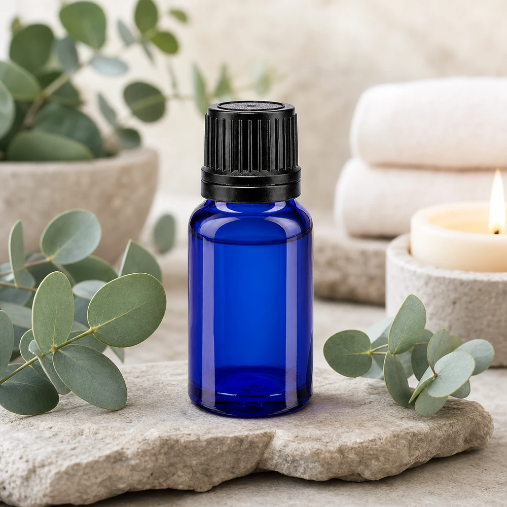 Blå 10 ml droppflaska med svart skruvlock på natursten med eukalyptusgrenar