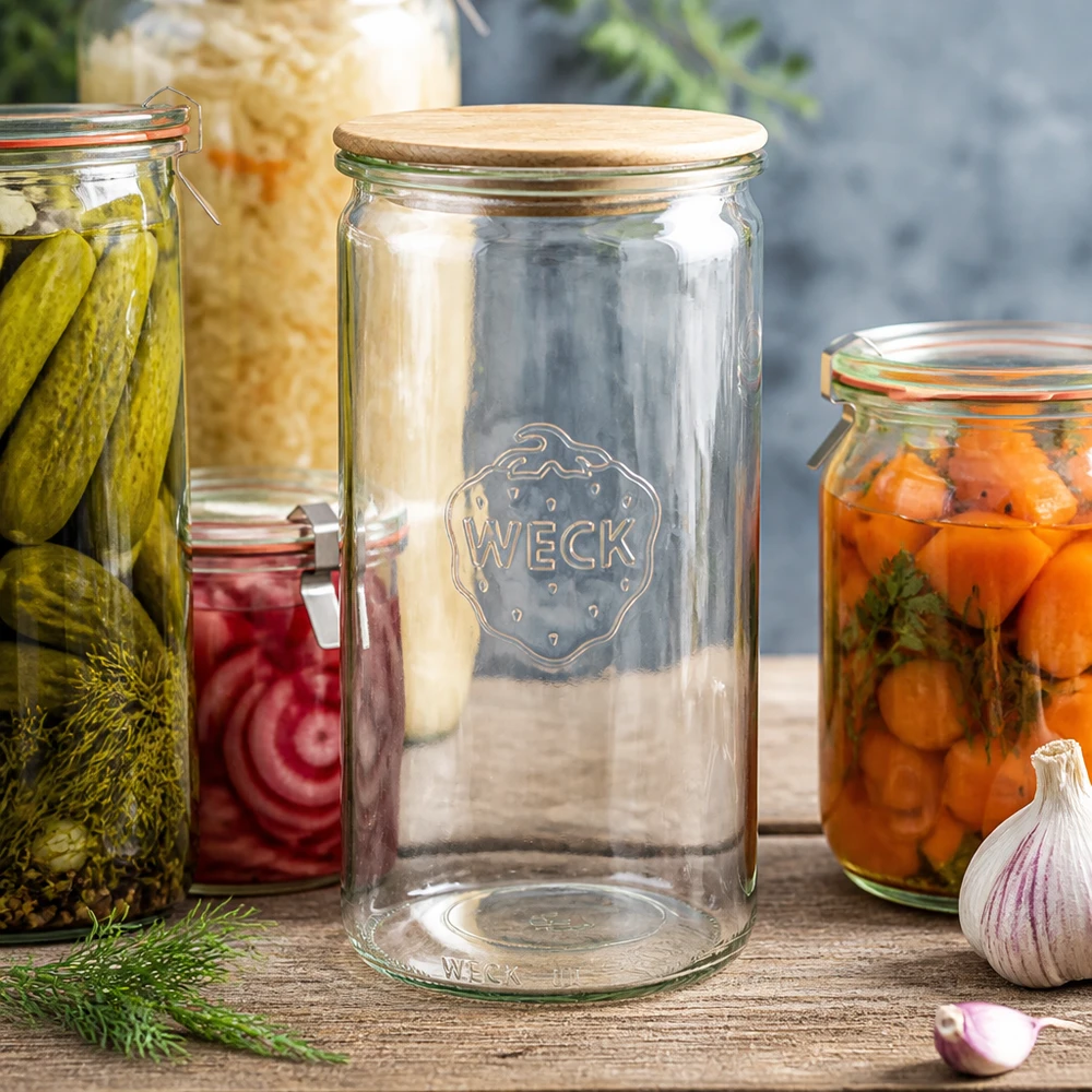 1590ml cylinderburk WECK RR100 med trälock WECK Zylinderglas 1590ml RR100 mit Holzdeckel zwischen Einmachgläsern mit Gurken Karotten und Sauerkraut auf Holztisch