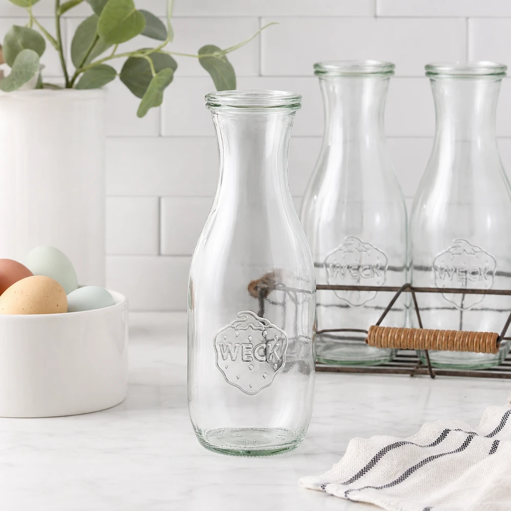 1062 ml juiceflaska med glaslock WECK RR60 WECK juiceflaska 1062ml glasflaska tom i modernt vitt kök med trådkorg i äggskal och växt