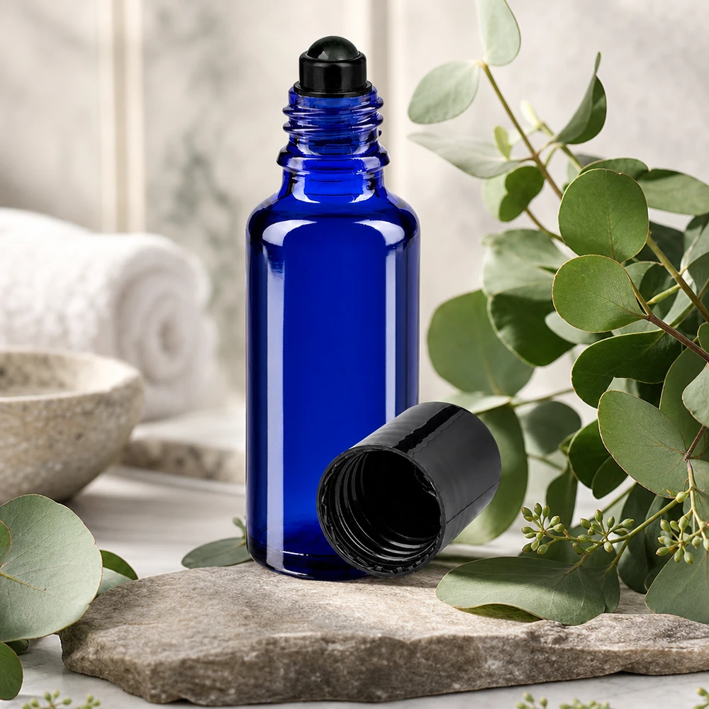 Apoteksflaska blå 30ml roll-on lock svart Koboltblå glasflaska på 30 ml med svart roll-on-huvud på natursten mellan eukalyptusgrenar