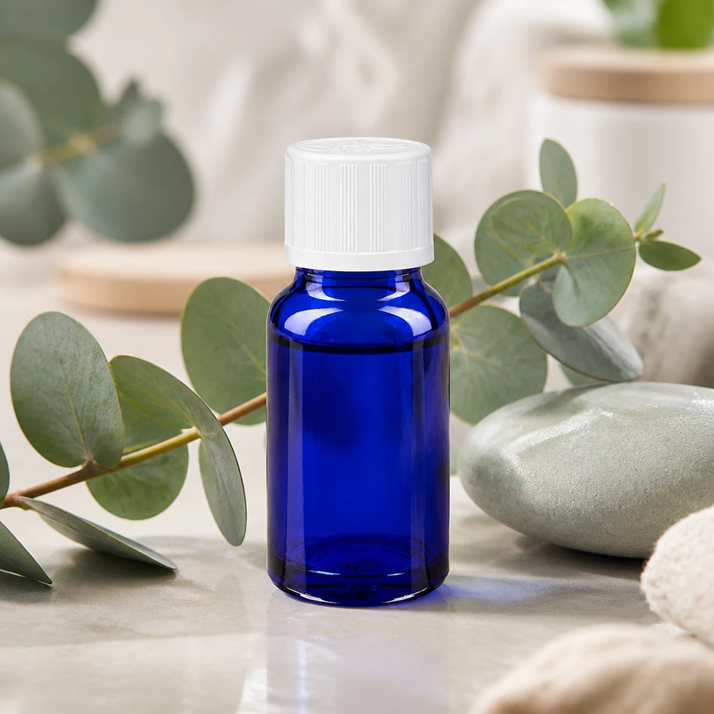 Apoteksflaska blå 10ml dropplock vit barnskyddande standard Koboltblå 10 ml apoteksflaska med vit KiSi-kork framför eukalyptusgrenar på marmor