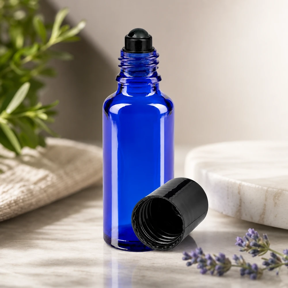 Apoteksflaska blå 30ml roll-on lock svart En koboltblå 30 ml glasflaska med rullapplikator och svart lock bredvid en lavendel- och en rosmarinkvist