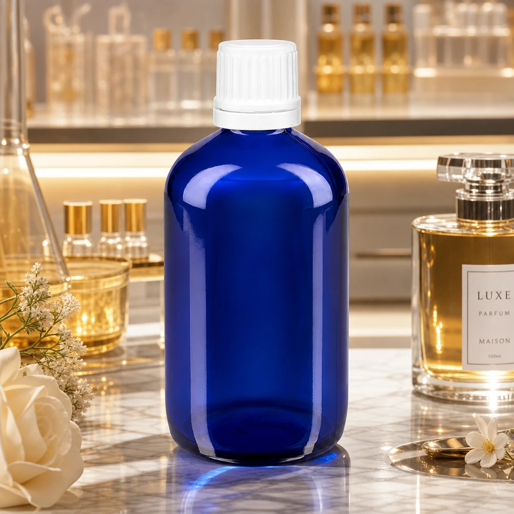 Apoteksflaska blå 100ml skruvkork vit manipulationsskyddad förslutning Blå apotekarflaska i glas, 100 ml, med vit OV-kork (11 mm) på marmor bredvid en lyxparfym