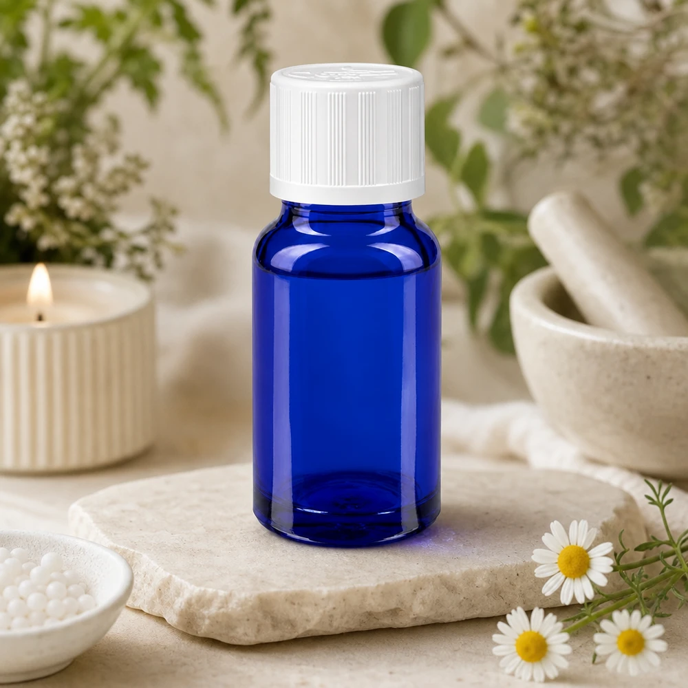 Apoteksflaska blå 10ml skruvkork vit barnsäker standard Blå apoteksflaska på 10 ml med vitt KiSi-lock på en stenplatta bredvid kamomillblommor
