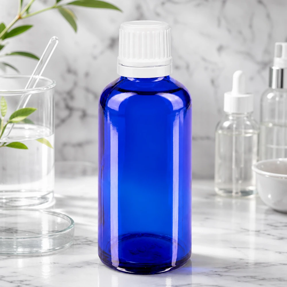 Apoteksflaska blå 50ml droppflaska 1,2mm vit barnsäker förslutning Liten blå glasflaska med droppkork på en marmorplatta, omgiven av laboratorieutrustning och växter