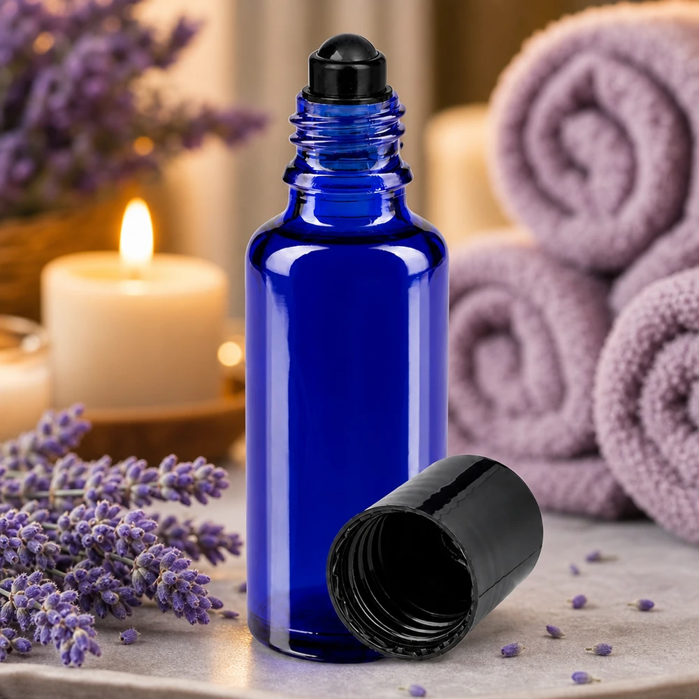 En koboltblå 30 ml roll-on-flaska av apotekerglas med svart lock bredvid lavendelblommor och ljus