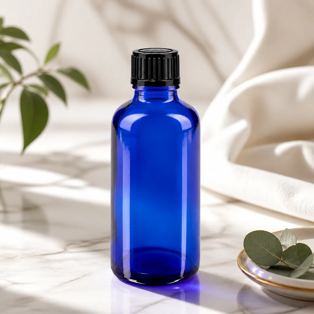 Apoteksflaska blå 50ml skruvkork svart standard Blå glasflaska på 50 ml med svart lock på marmor bredvid eukalyptusblad