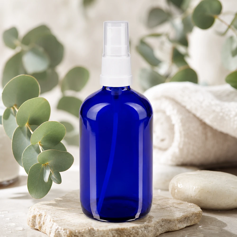 Rund 100 ml sprayflaska av blått UV-skyddsglas med vit pumpfördelare på natursten