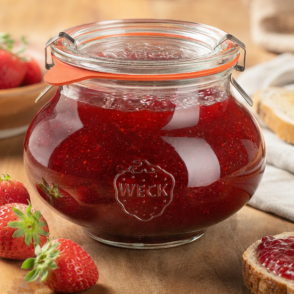 WECK dekorativ burk 560ml fylld med hemgjord jordgubbssylt, med stängt lock, omgiven av färsk frukt och grönsaker.