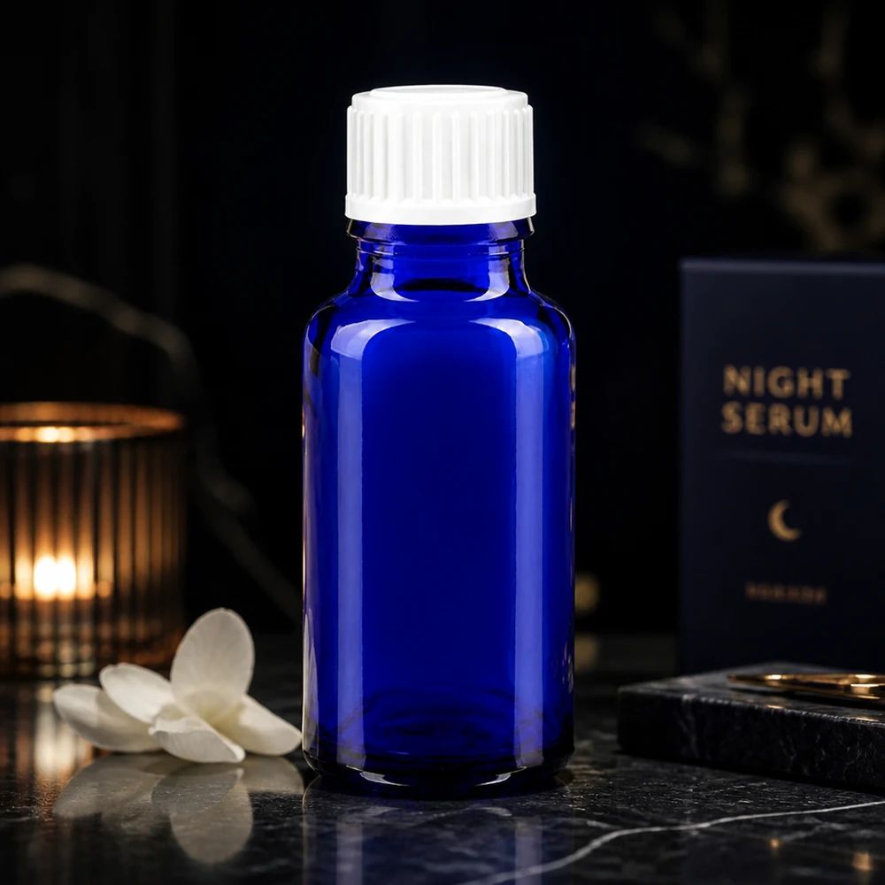 Apoteksflaska blå 20ml skruvkork vit standard En koboltblå glasflaska på 20 ml med vitt lock bredvid förpackningen till Night Serum på en mörk bakgrund