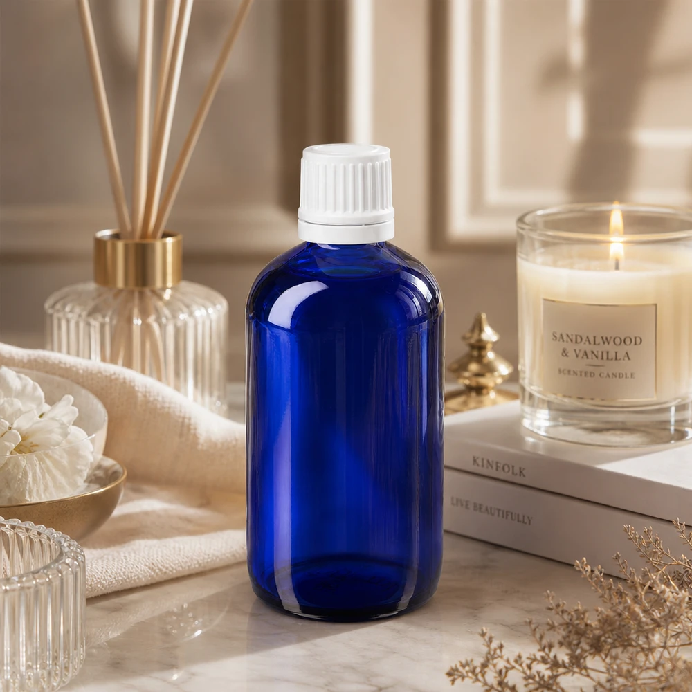 Apoteksflaska blå 100ml skruvkork vit manipulationsskyddad förslutning Blå apoteksflaska i glas, 100 ml, med barnsäker vit lock på marmor bredvid ett sandelträ-ljus