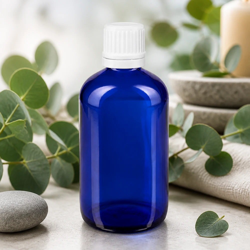 Apoteksflaska blå 100ml droppflaska 1.2mm vit barnsäker förslutning Apoteksflaska, 100 ml, i blått med vit droppflaska mellan eukalyptusgrenar och spa-stenar