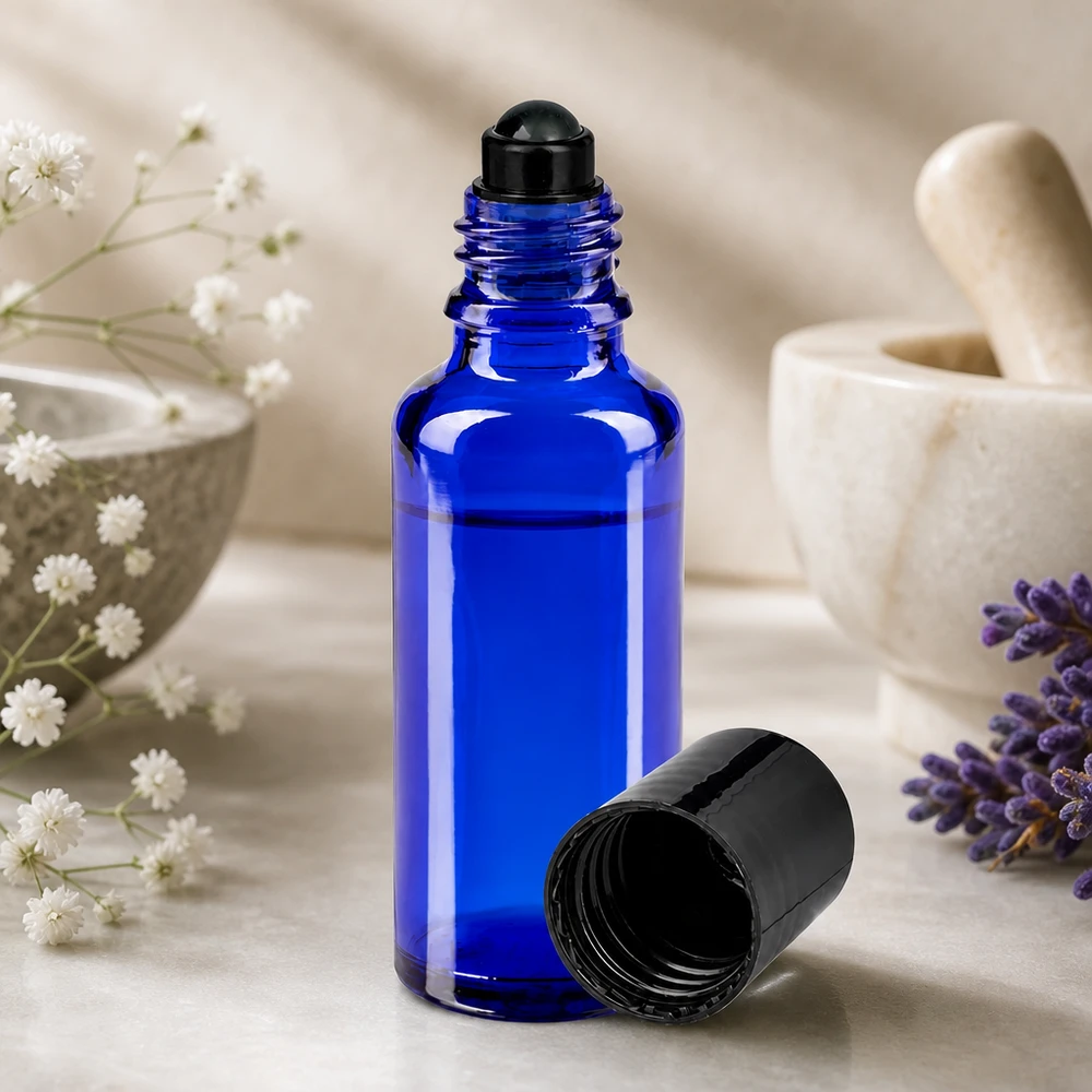 Blå 30 ml apotekarflaska med rullkula i svart bredvid lavendel och mortel