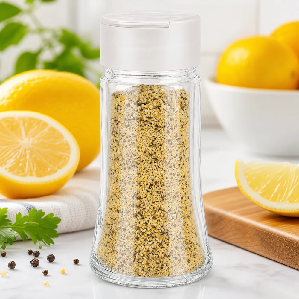 Citronpeppar i ett genomskinligt kryddglas på 95 ml med vitt lock med dubbla ströare, framför färska citroner
