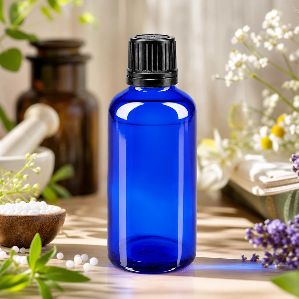 Blå apotekarflaska på 50 ml med svart originalförslutning, omgiven av lavendel och kamomillblommor