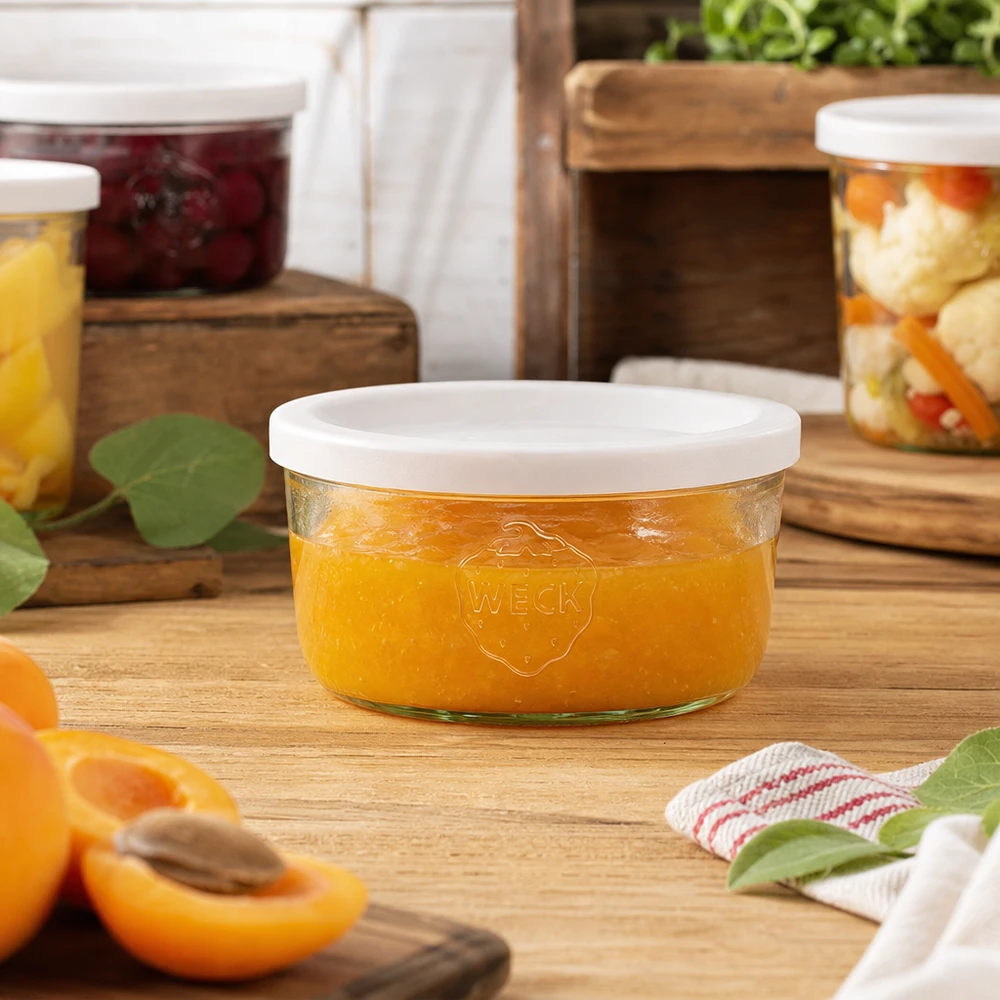 165ml Krossade glasögon med lock WECK RR80 WECK 165 ml murarburk fylld med apelsinmarmelad i en naturlig köksmiljö med konserveringsburkar i bakgrunden