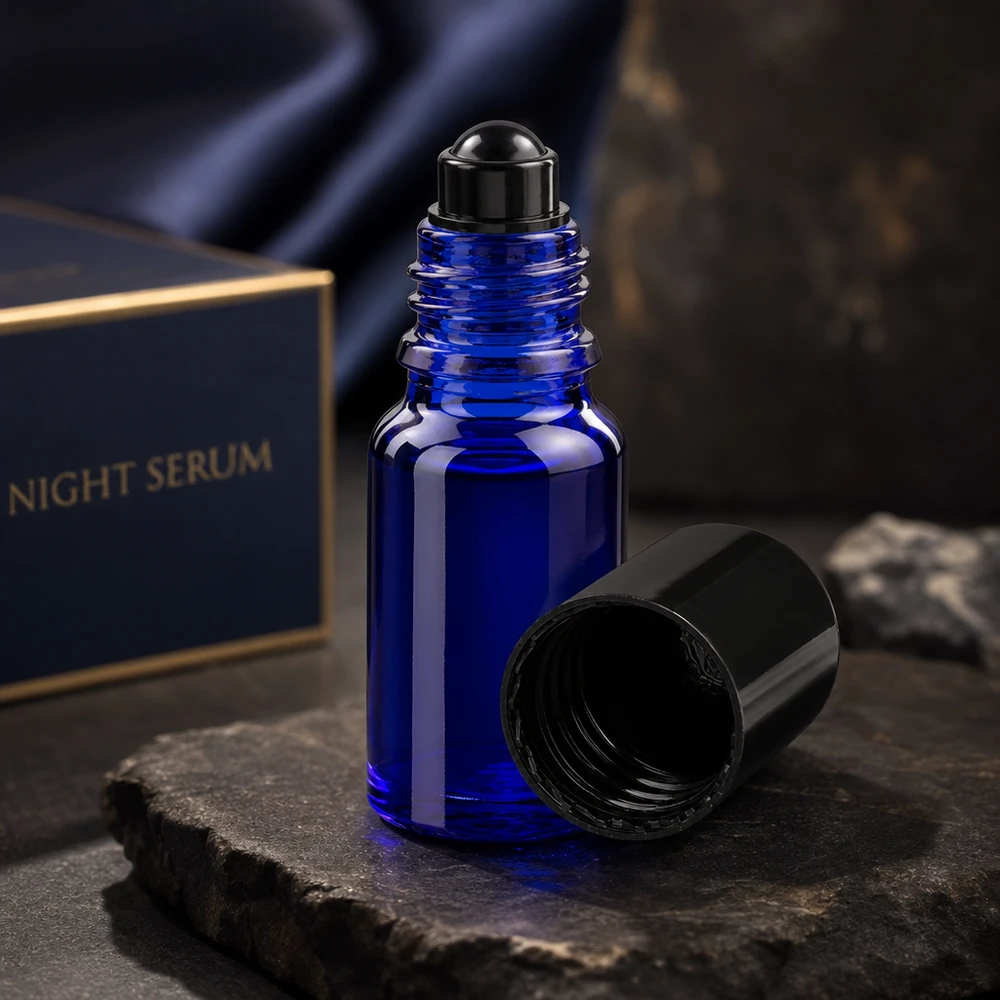 Apoteksflaska blå 10ml roll-on lock svart Mörkblå 10 ml ApoGlas-roll-on-flaska med öppet svart lock på en skiffersten framför en Night Serum-låda