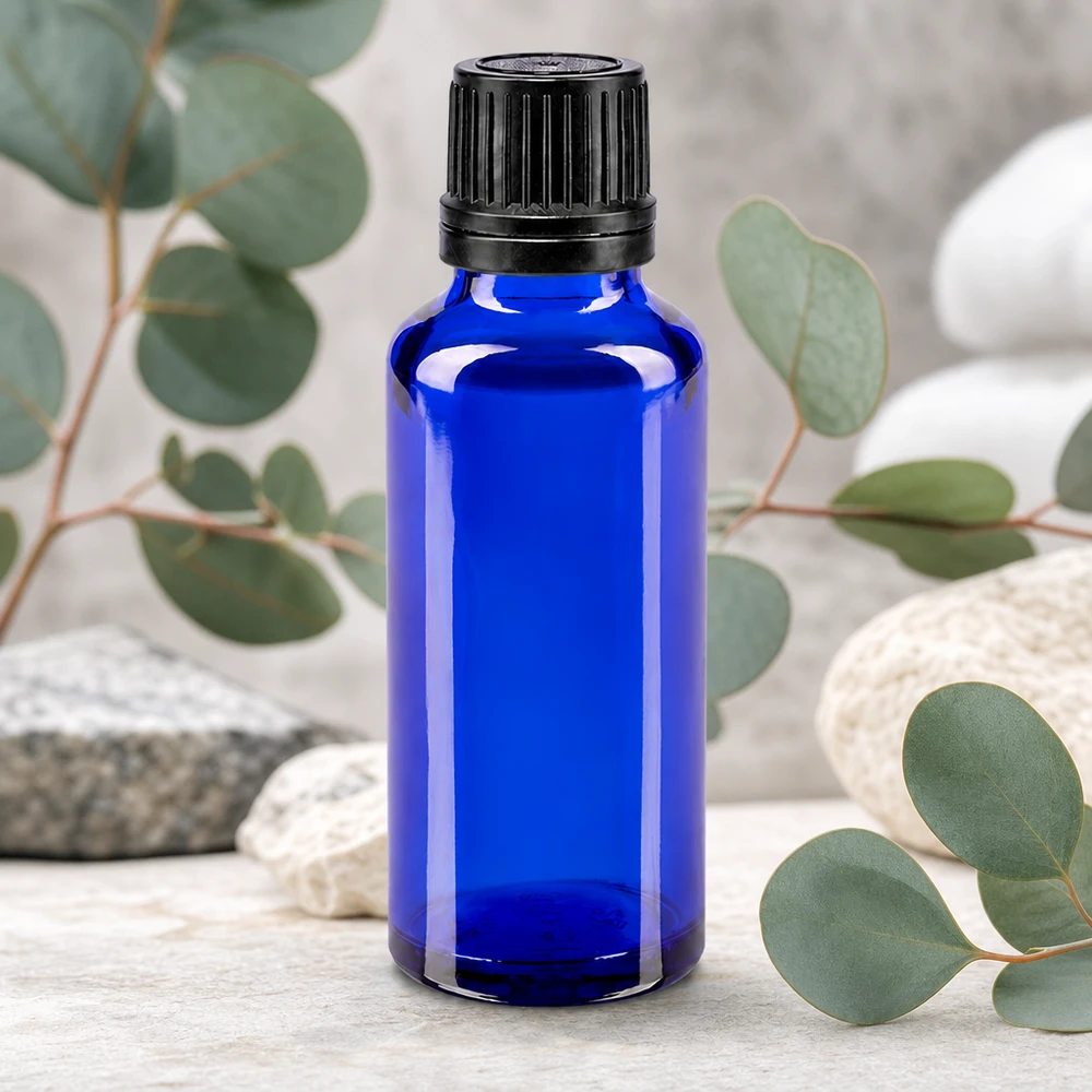Liten blå glasflaska på 30 ml med svart originalförslutning framför eukalyptusgrenar