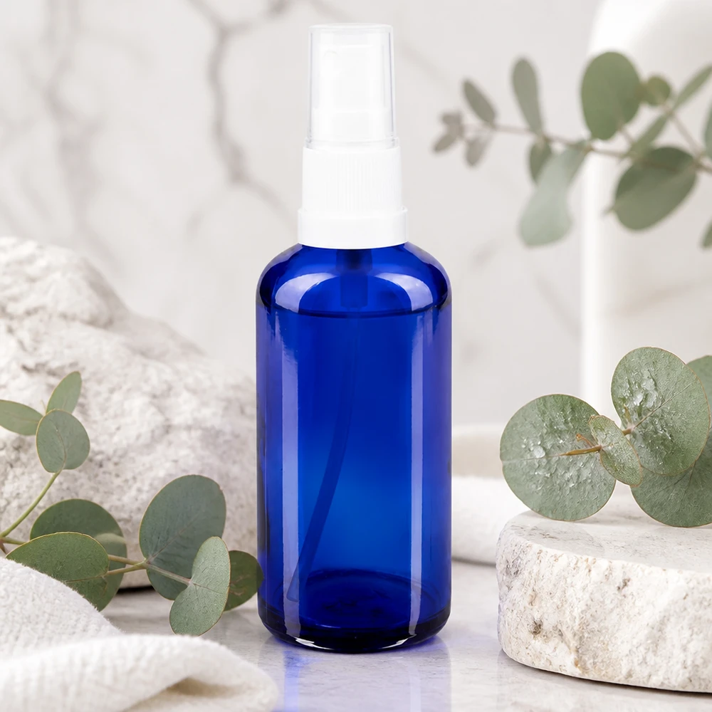 50 ml blå glasflaska med sprayhuvud i vitt på marmor med eukalyptus