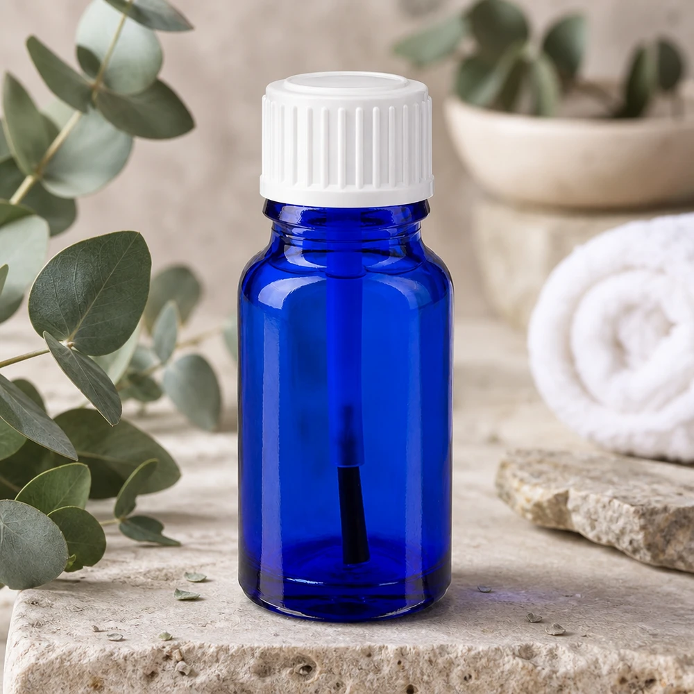 Apoteksflaska blå 10ml skruvlock vit borste Blå glasflaska på 10 ml med vit penselmunstycke bredvid eukalyptusgrenar på natursten