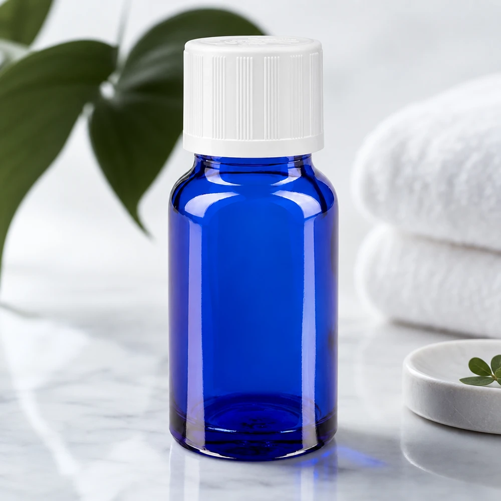 Apoteksflaska blå 10ml dropplock vit barnskyddande standard 10 ml blått apotekerglas med vitt barnsäkert lock på en marmoryta bredvid vikta handdukar